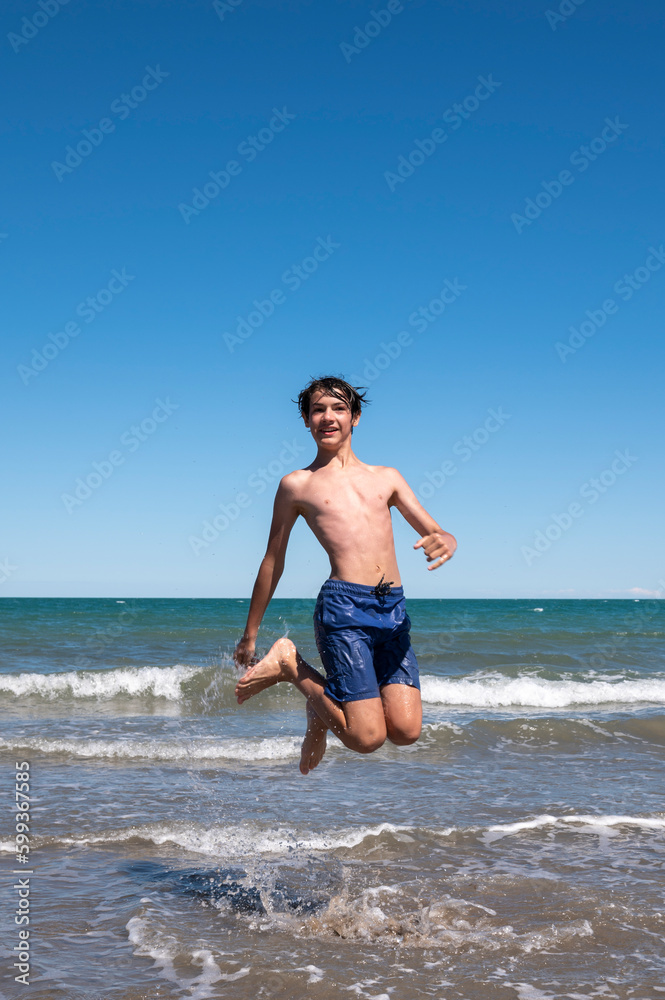Boy happily enjoying the sea on his summer vacation, doing big jumps on the shore of the beach.
