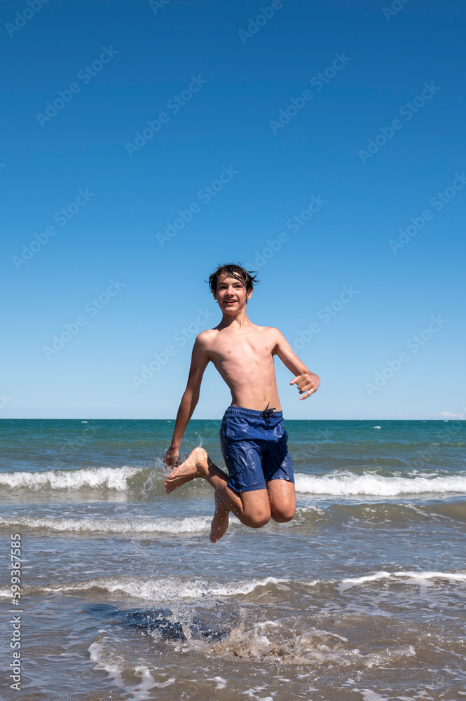 Boy happily enjoying the sea on his summer vacation, doing big jumps on the shore of the beach. Boy happily enjoying the sea on his summer vacation, doing big jumps on the shore of the beach.