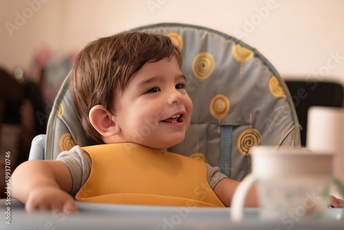 Little boy smiling and having fun while sitting in his high chair at home. Childhood concept.