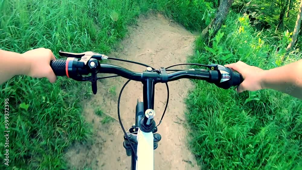 Man riding bicycle on dirt path in forest on sunny summer day. POV. Person cycling bicycle along path between green trees in wood. Extreme lifestyle activity entertainment active Man riding bicycle on dirt path in forest on sunny summer day. POV. Person cycling bicycle along path between green trees in wood. Extreme lifestyle activity entertainment active