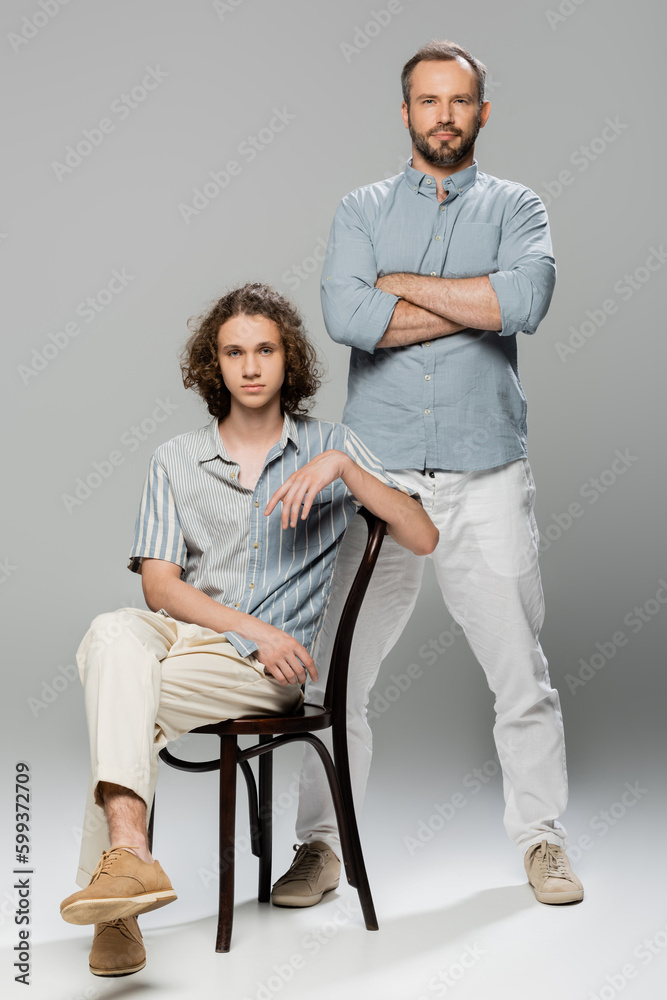 full length of good looking man standing with folded arms near teenage son on grey. full length of good looking man standing with folded arms near teenage son on grey.