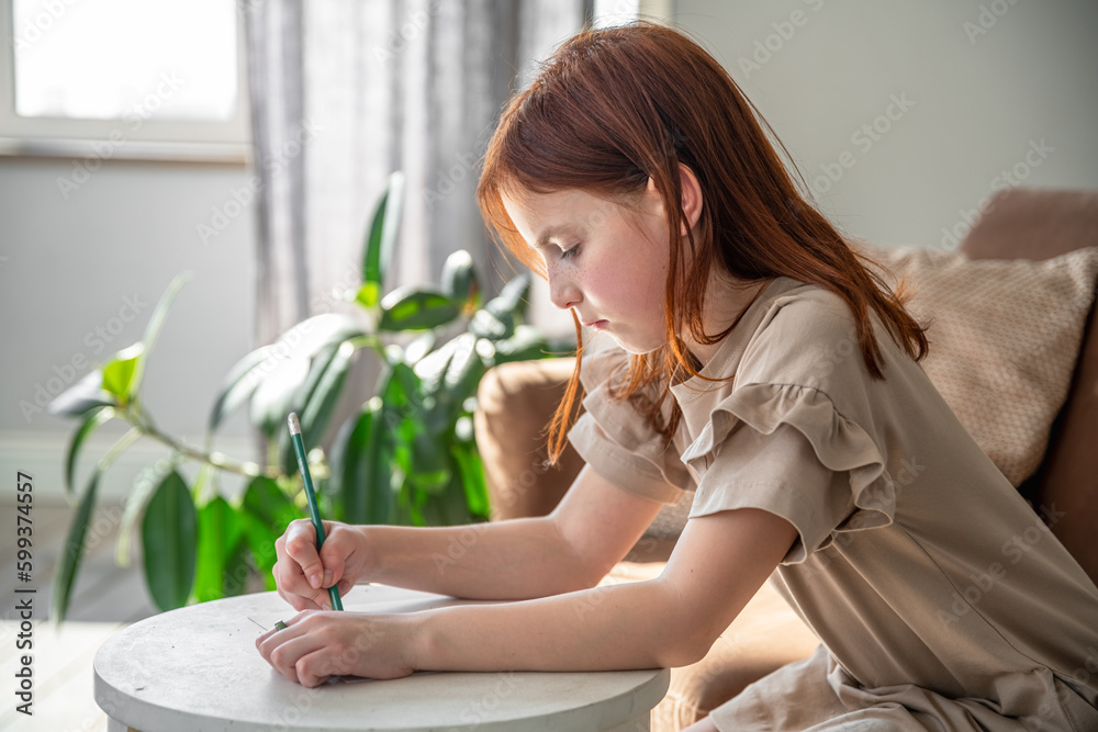 Obraz premium cute little preteen girl drawing with pen while sitting at desk at home, beautiful female child, small kid doing school homework