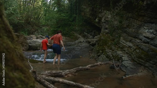 Boy and mother walking among rocks in cold stream. Creative. Hiking in wild nature.