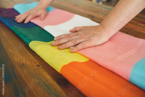 Side view of a woman's hands folding a rainbow and a gender queer flag, symbols of Pride Month