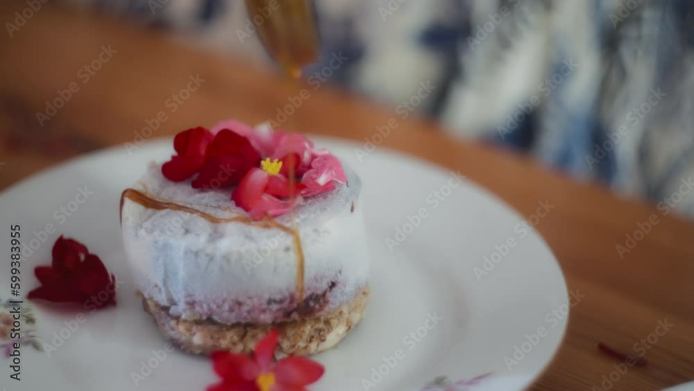 Honey being poured on a gourmet dessert with edible flowers. Slow motion, shallow depth of field. 