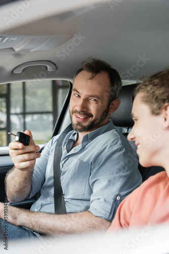 cheerful and bearded man holding car key next to son in modern auto.