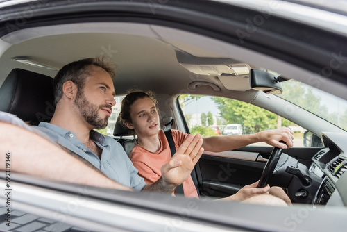 bearded dad pointing while showing direction to teenage son driving car.