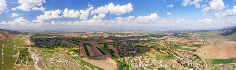 Aerial panorama of patchwork fields with shadows cast by clouds and a rural settlement