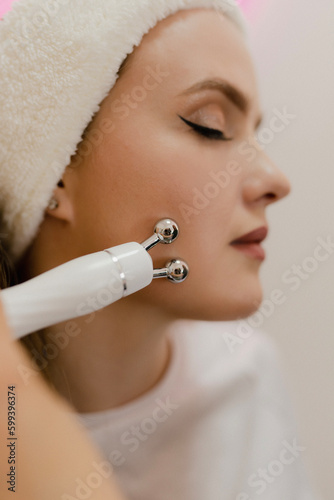 A beautiful young girl in a beauty salon on a facial rejuvenation procedure smiles while a master cosmetologist makes her skin lifting close-up
