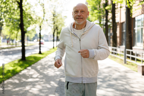 Fototapeta Naklejka Na Ścianę i Meble -  Portrait of the smiled mature man running and wearing headphones in the street. Sport and healthy lifestyle concept