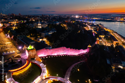 Picturesque night view of illuminated St. George Tower and walls of Nizhny Novgorod Kremlin on bank of Volga river on background with modern cityscape in summer, Russia photo