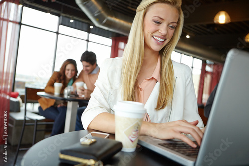 Blogging on the go. A beautiful young woman using her laptop in a busy coffee shop.