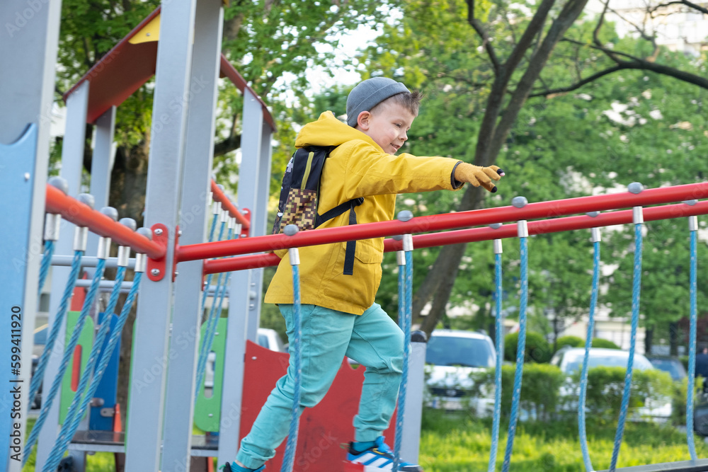 Portrait of six year old boy in yellow jacket playing on playground..