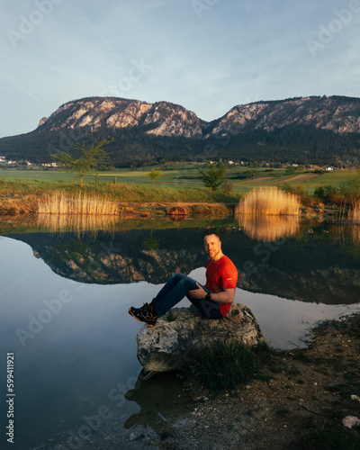 person sitting on a rock at a lake with mountain in background 