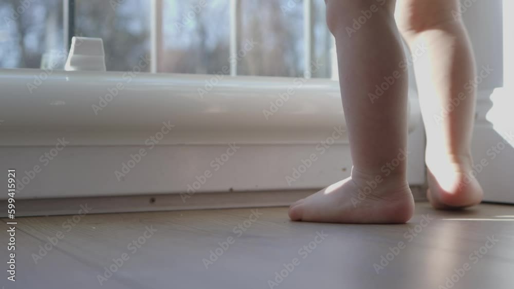 tiny barefoot legs baby child doing first steps, learning balancing stand still near window. Daytime sun beams light little toddler toes and heels. baby learn to walk stand on tip toes wooden floor. tiny barefoot legs baby child doing first steps, learning balancing stand still near window. Daytime sun beams light little toddler toes and heels. baby learn to walk stand on tip toes wooden floor.