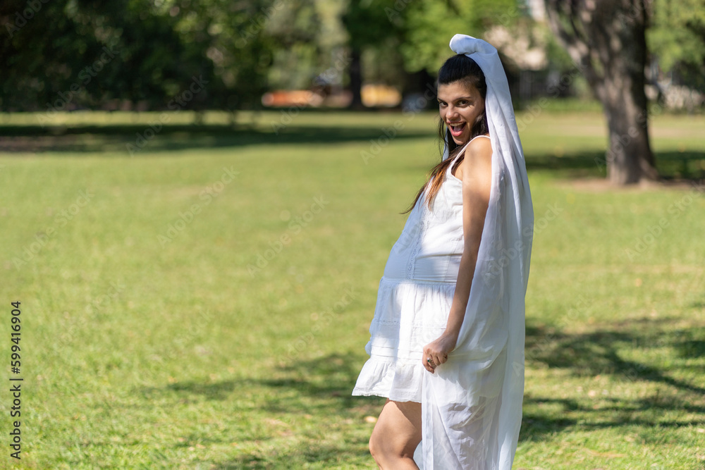 Pregnant bride in a white wedding dress holds her belly with her hand in a park. Seductive expression Pregnant bride in a white wedding dress holds her belly with her hand in a park. Seductive expression