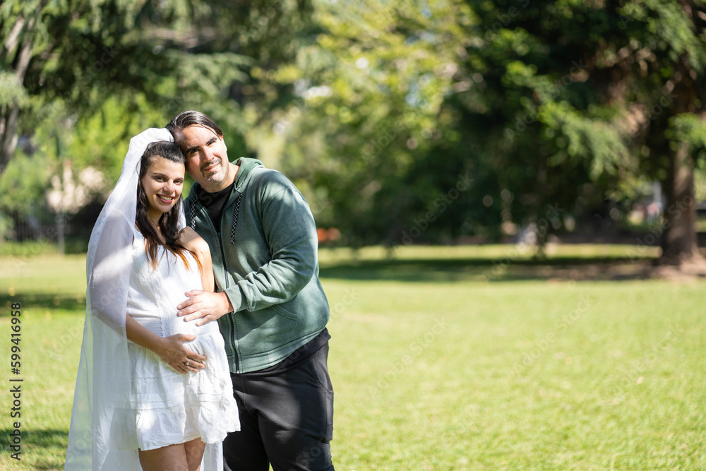 Pregnant woman in wedding dress posing with her partner outdoors Pregnant woman in wedding dress posing with her partner outdoors