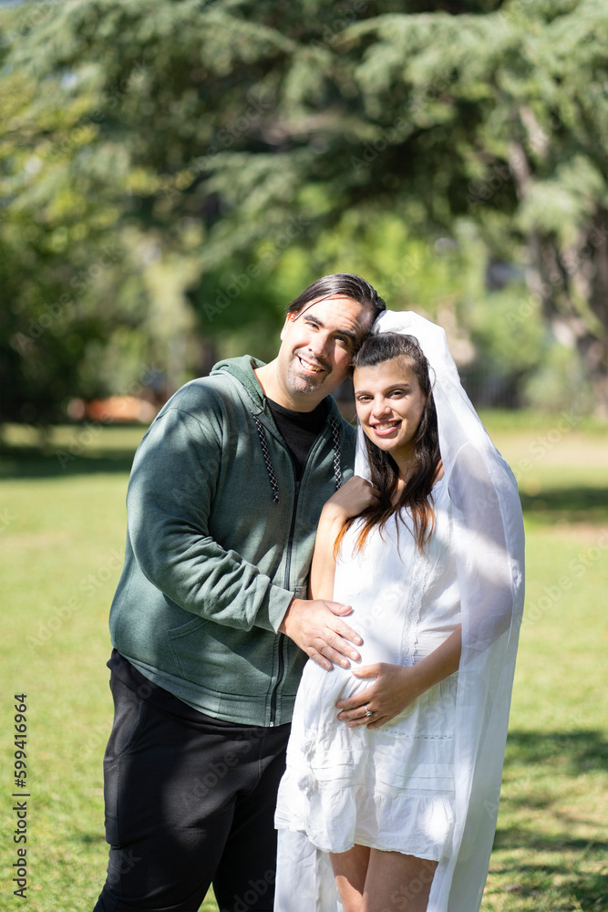 Pregnant woman in wedding dress posing with her partner outdoors Pregnant woman in wedding dress posing with her partner outdoors