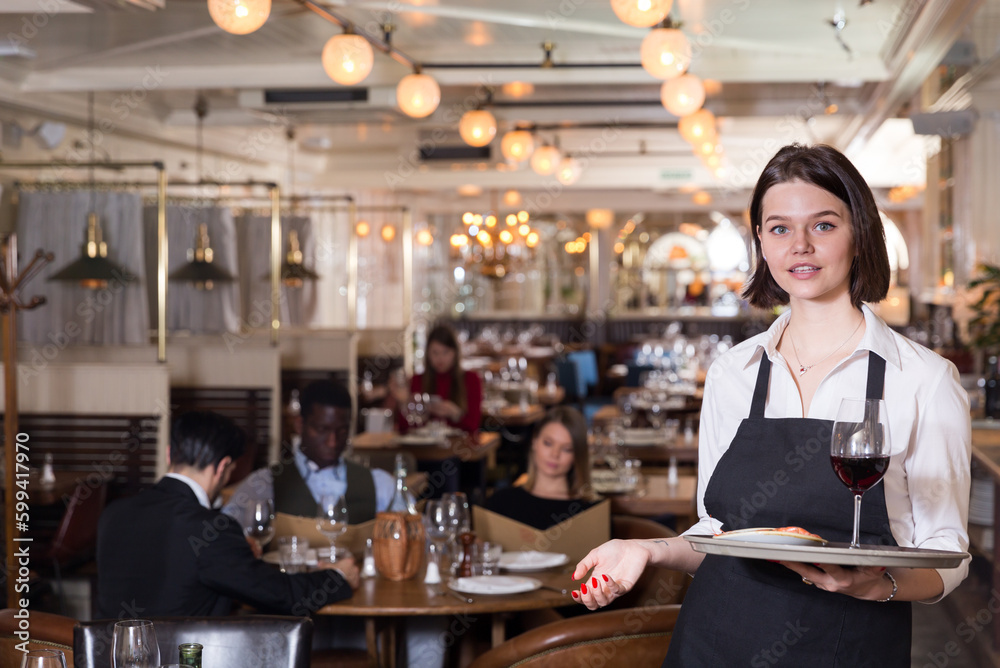 Attractive young waitress with serving tray welcoming in restaurant