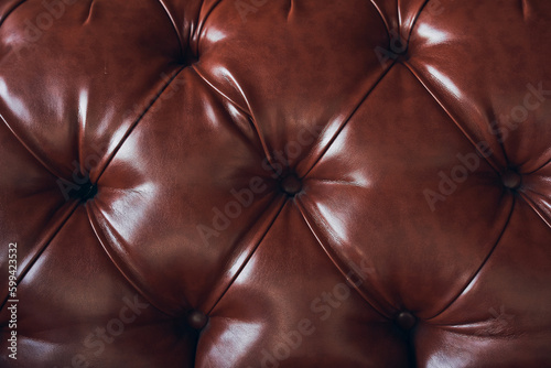 The texture of the background is a close-up of brown genuine leather, upholstered furniture in retro Chesterfield style with a deep diamond pattern and buttons. High quality photo