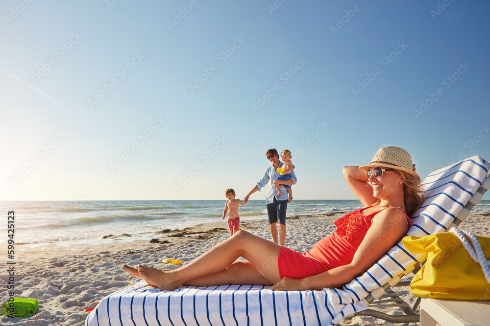 Dad is on duty on weekends. a woman lying on a lounger at the beach with her family in the background.