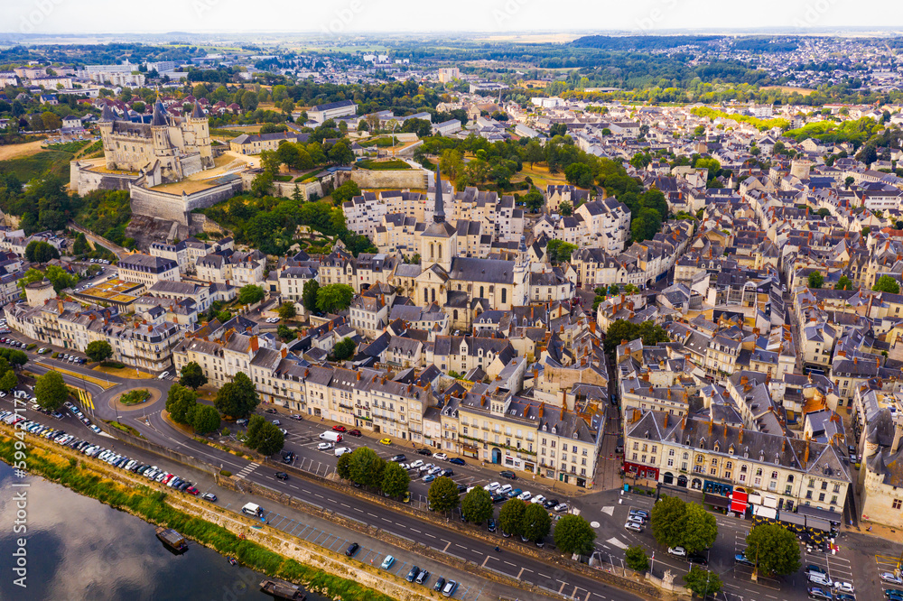 General summer view of picturesque French commune of Saumur on Loire banks looking out over medieval fortified Chateau and spire of catholic parish church