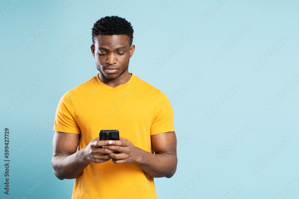 Portrait of serious Nigerian man holding mobile phone, reading text message, communication online isolated on blue background. Handsome African guy shopping online, choosing on website. Technology Portrait of serious Nigerian man holding mobile phone, reading text message, communication online isolated on blue background. Handsome African guy shopping online, choosing on website. Technology