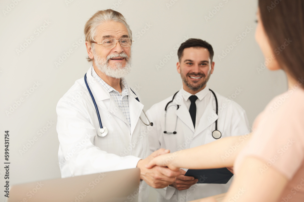 Happy senior doctor shaking hands with patient in clinic Happy senior doctor shaking hands with patient in clinic