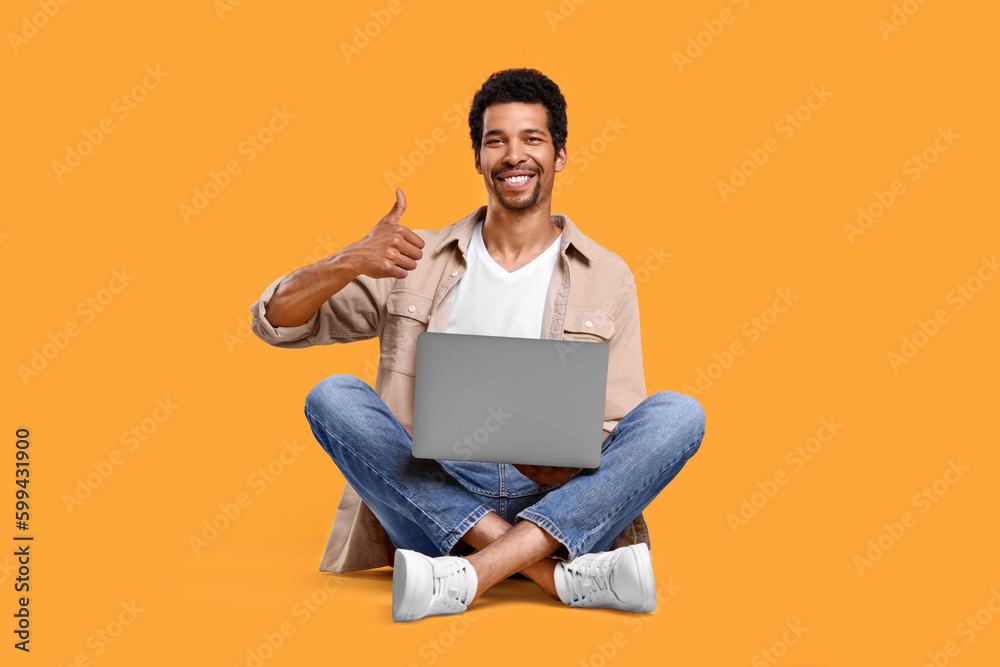 Happy man with laptop showing thumb up against orange background