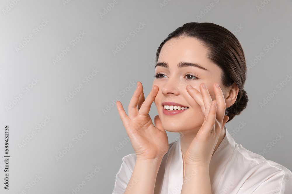 Young woman massaging her face on grey background. Space for text Young woman massaging her face on grey background. Space for text