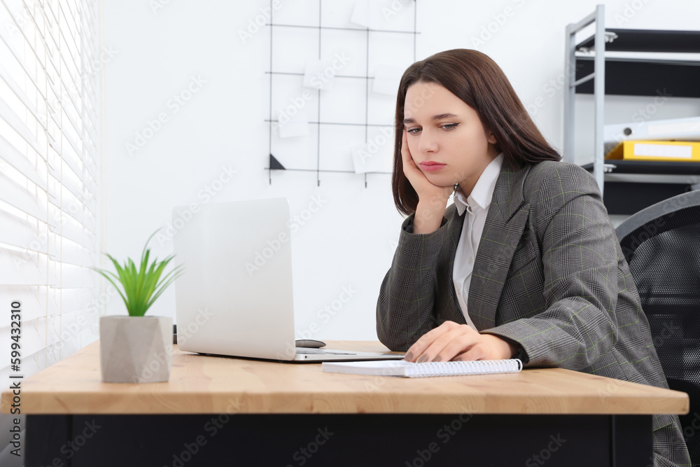 Puzzled young intern using laptop at table in modern office. First work day Puzzled young intern using laptop at table in modern office. First work day