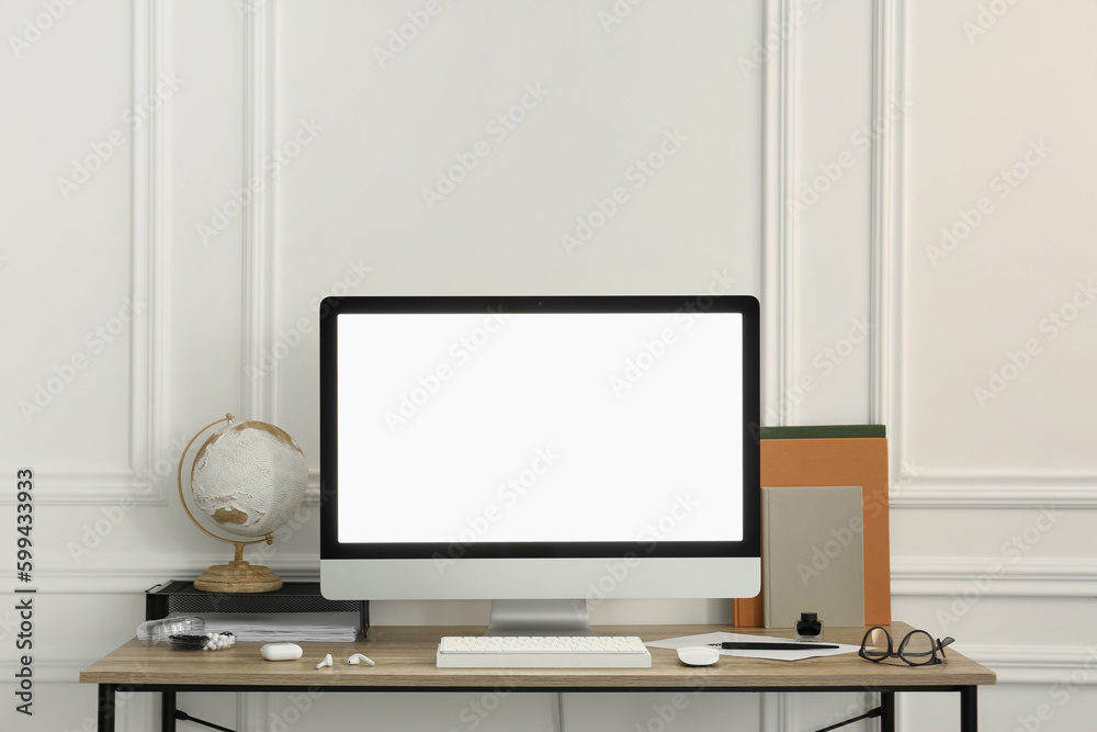 Stylish workspace with computer and stationery on wooden desk near white wall Stylish workspace with computer and stationery on wooden desk near white wall