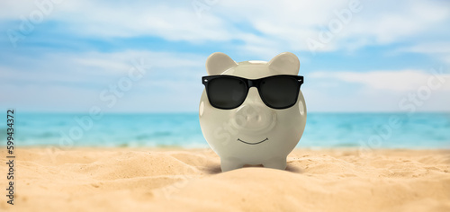 Vacation savings. Piggy bank with sunglasses on sandy beach near sea, banner design