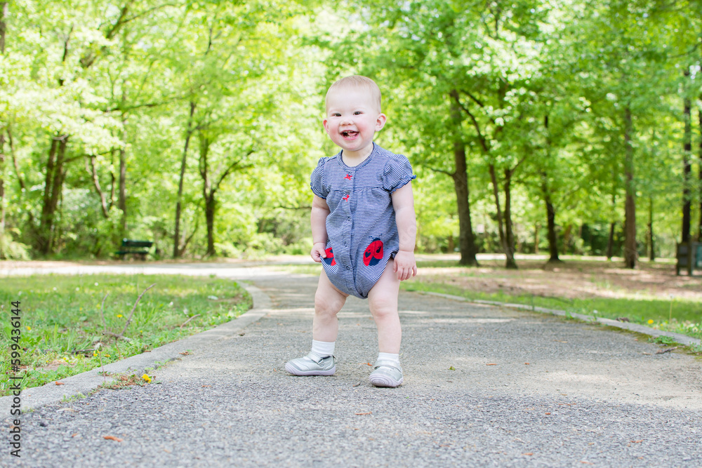 A Toddler is taking her first steps in the park. Baby is learning how to walk. Baby development 1-year-old girl A Toddler is taking her first steps in the park. Baby is learning how to walk. Baby development 1-year-old girl