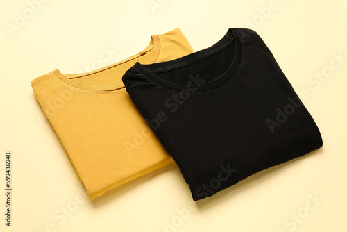 Folded yellow and black t-shirts on color background