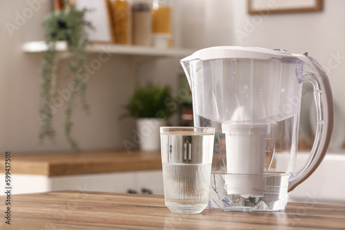 Glass of pure water and filter jug on wooden table in kitchen