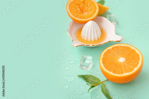 Juicer with orange slices, ice cubes and mint on turquoise background