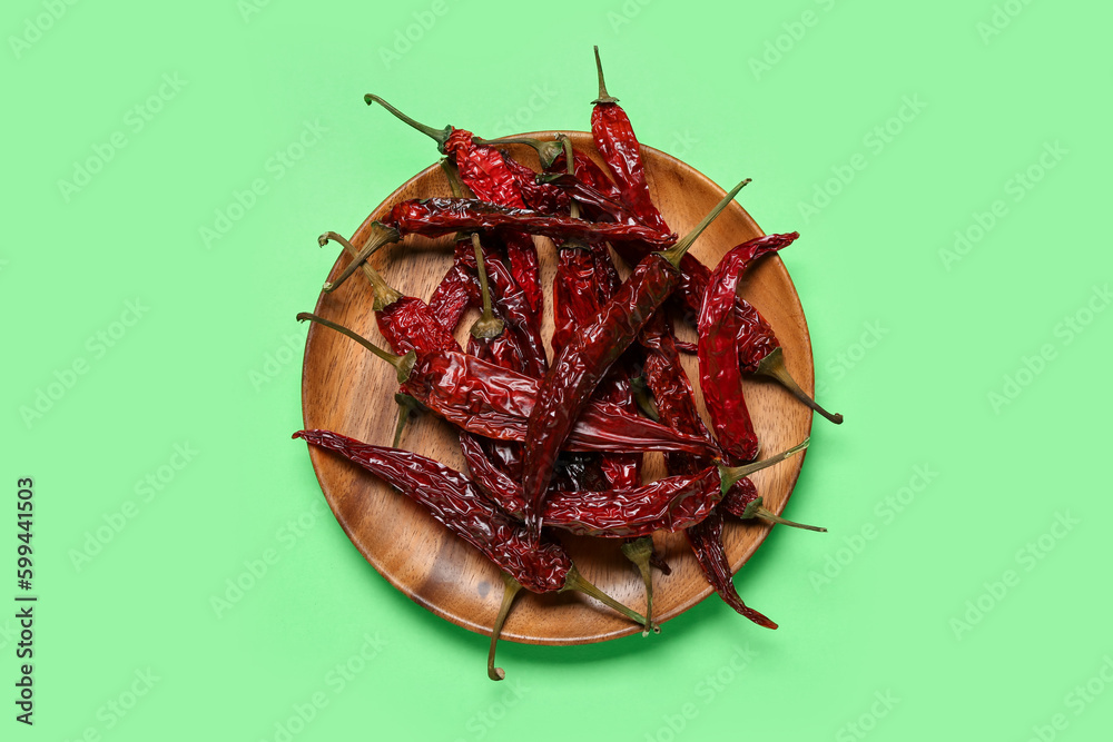 Fototapeta premium Wooden plate with Dry hot chili peppers on pale green background