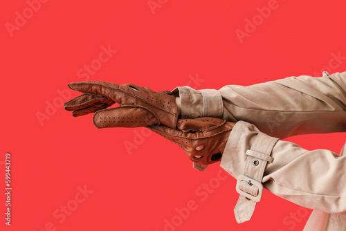 Hands of young woman in leather gloves on red background