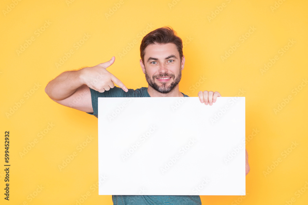 Man with blank banner isolated on studio background. Portrait of attractive man with empty blank poster. Man showing poster, pointing finger on signboard placard. Male presenting billboard or banner. Man with blank banner isolated on studio background. Portrait of attractive man with empty blank poster. Man showing poster, pointing finger on signboard placard. Male presenting billboard or banner.