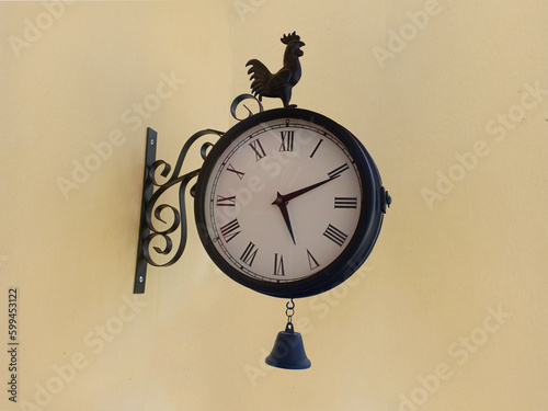 Old vintage clock face with roman number decorated with chicken and bell attatched on yellow wall background