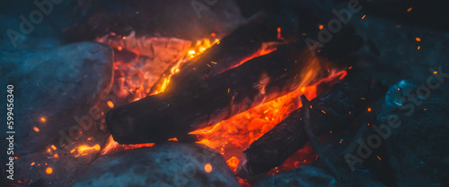 Vivid smoldered firewoods burned in fire close-up. Atmospheric background with orange flame of campfire. Unimaginable full frame image of bonfire. Glowing embers in air. Warm logs, bright sparks bokeh