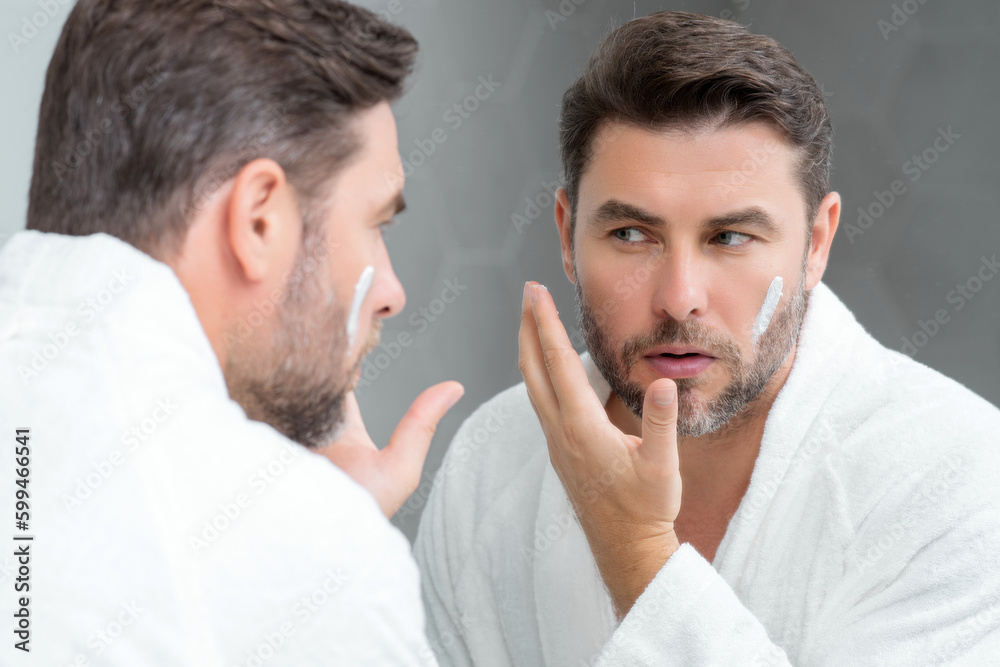 Fototapeta premium Skin care. Beauty middle aged man applying face cream. Male spa hold face cream. Facial cream, moisturizing lifting nourishing creme. Face cream for skincare. Wrinkle cosmetic facial treatment.