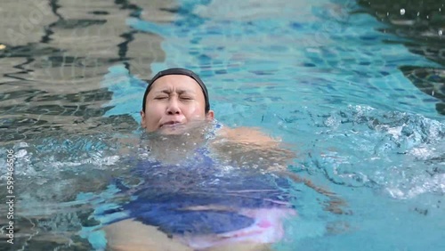 Young Asian woman drowning due to leg cramp in swimming pool area
