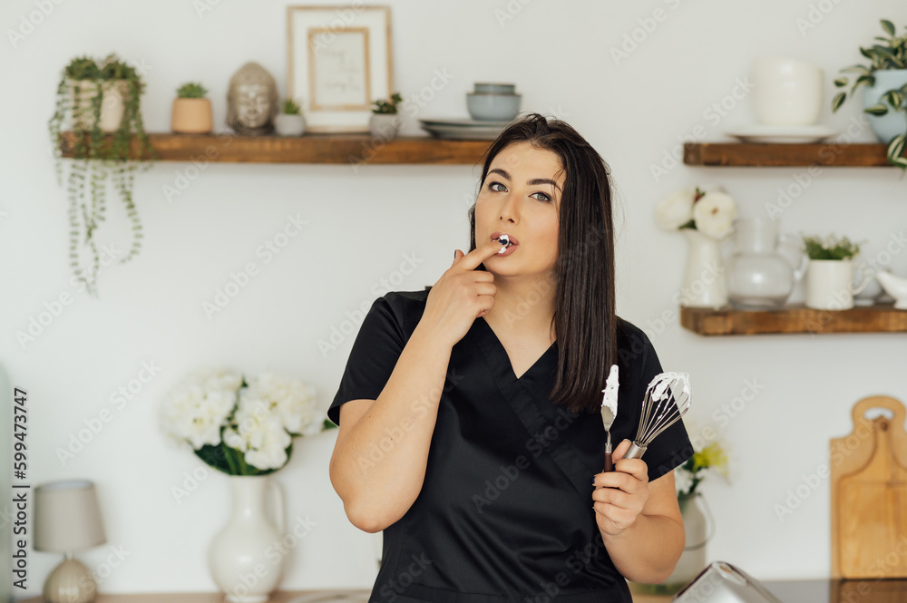 Woman cook tastes the cream for cakes whipped in a mixer Woman cook tastes the cream for cakes whipped in a mixer