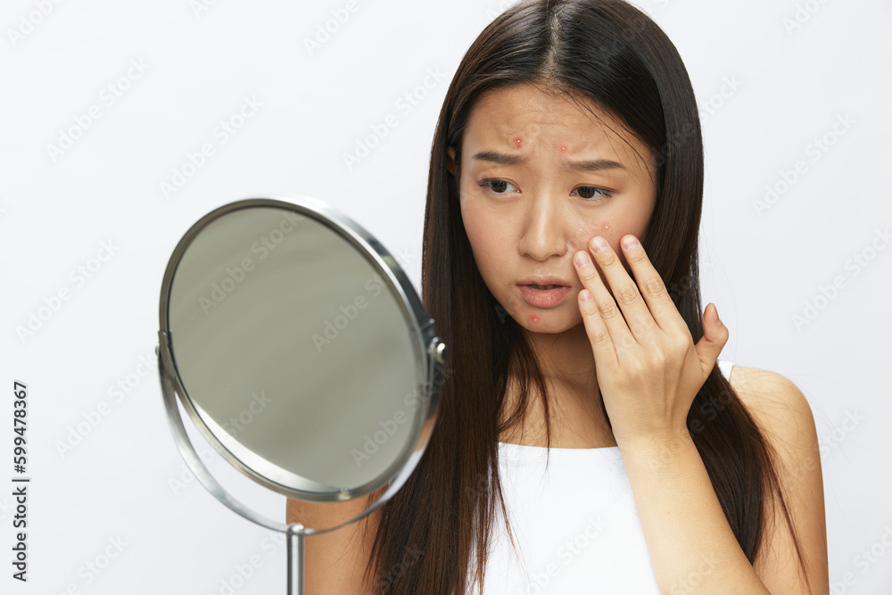 Asian woman with mirror in hand facial skin problems, acne and inflammation, red rash and allergies, chicken pox, sadness from rashes. Facial skin care concept for diseases and nerves Asian woman with mirror in hand facial skin problems, acne and inflammation, red rash and allergies, chicken pox, sadness from rashes. Facial skin care concept for diseases and nerves