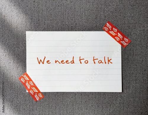 Note stick on office wallpaper with handwritten text - We Need To Talk  - concept of having difficult conversations to solve relationship conflict, workplace serious issues conflict discussion