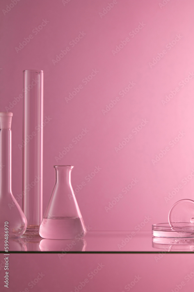 Several laboratory glassware containing transparent liquid are placed on a glass table with purple background. Blank space to display product Several laboratory glassware containing transparent liquid are placed on a glass table with purple background. Blank space to display product