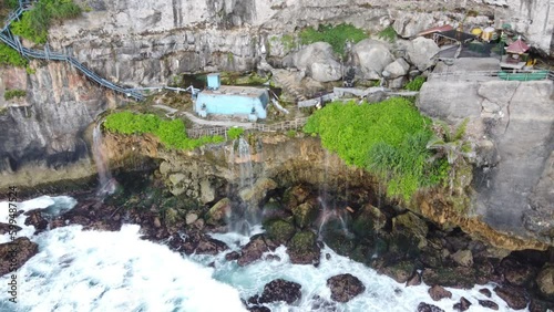 Aerial : Guyangan waterfall, Nusa Penida Island, Indonesia.
Also called Peguyangan fall. Waves crashing on cliffside rocks beneath blue water Tank, steep stairway, Temple and natural infinity pool. photo