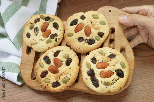 Hand Placing a Wooden Grid of Freshly Baked Almond and Raisin Cookies on the Table